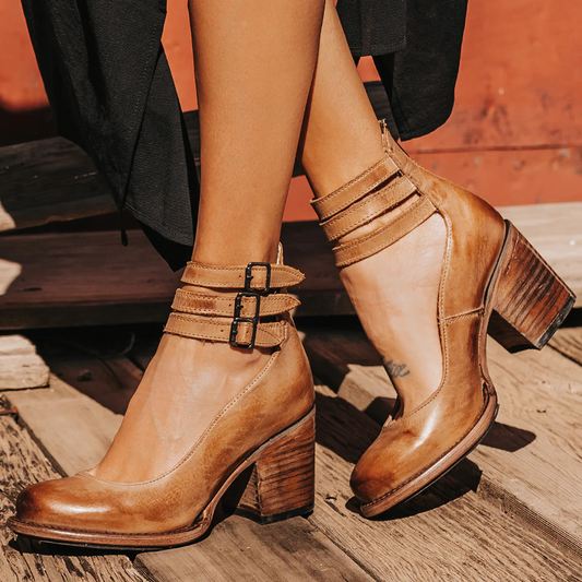 Braune Lederstiefeletten mit Blockabsatz und Schnallen, getragen von einer Person auf Holzboden. Modische Damenstiefel, ideal für Herbstoutfits.