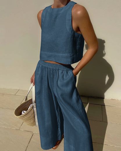Frau in blauem Leinen-Zweiteiler mit ärmellosem Top und weiten Hosen, hält eine Strohtasche. Sommermode, lässiger Stil, elegantes Outfit.