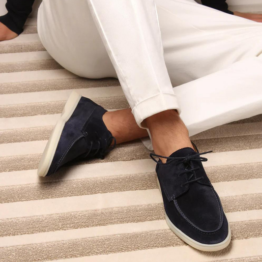 Dunkelblaue Wildleder-Sneaker auf gestreiftem Teppich, getragen von Person in weißen Hosen. Modische Herrenschuhe, lässiger Stil.