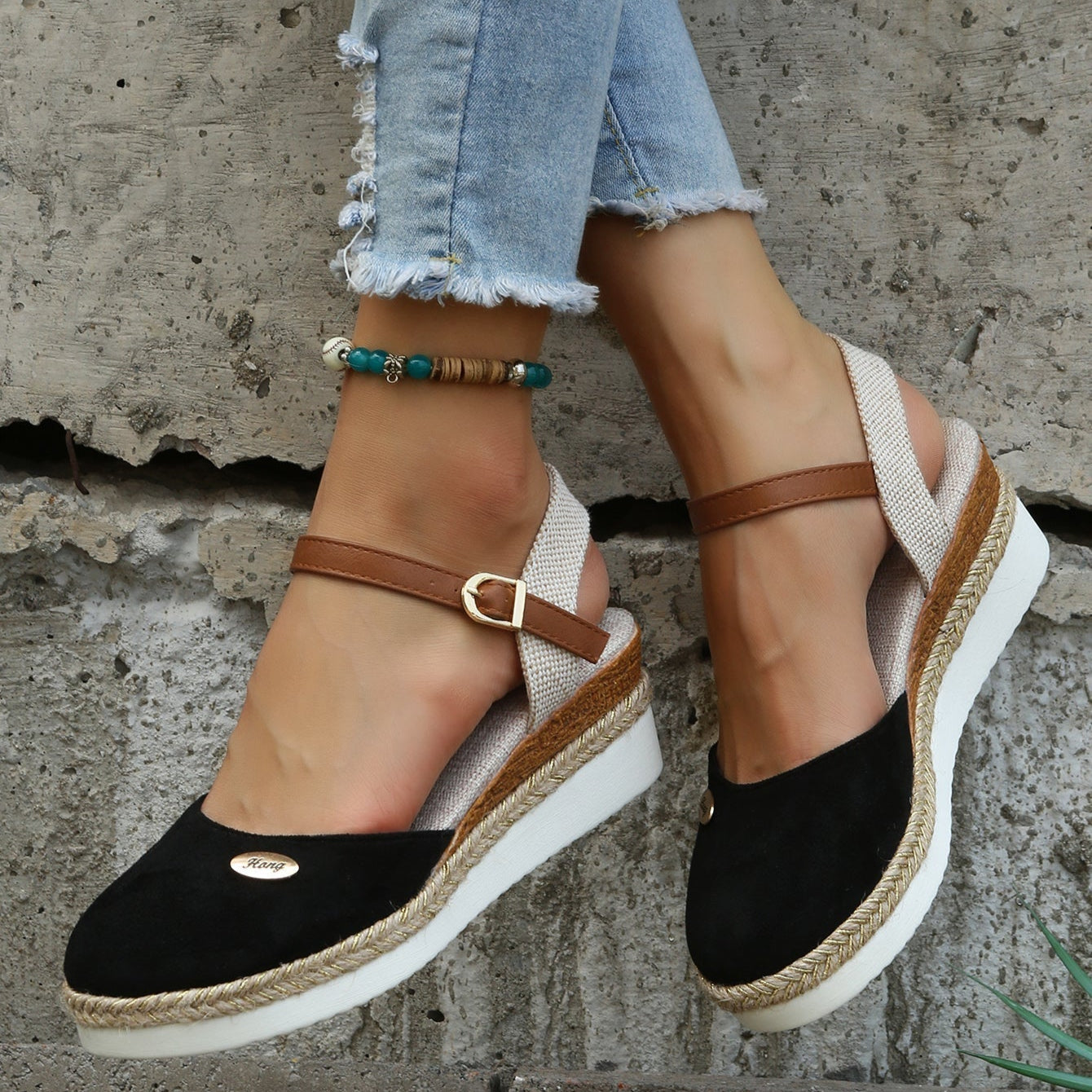 Damen Sandalen mit Keilabsatz, schwarzem Wildleder, braunen Riemen und geflochtener Sohle, kombiniert mit blauer Jeans und Fußkettchen.