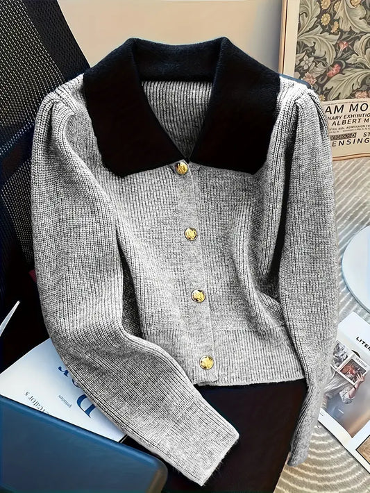 Grauer Strickpullover mit schwarzen Kragen und goldenen Knöpfen auf einem Stuhl. Modetrend, stilvolle Damenbekleidung, elegantes Design.