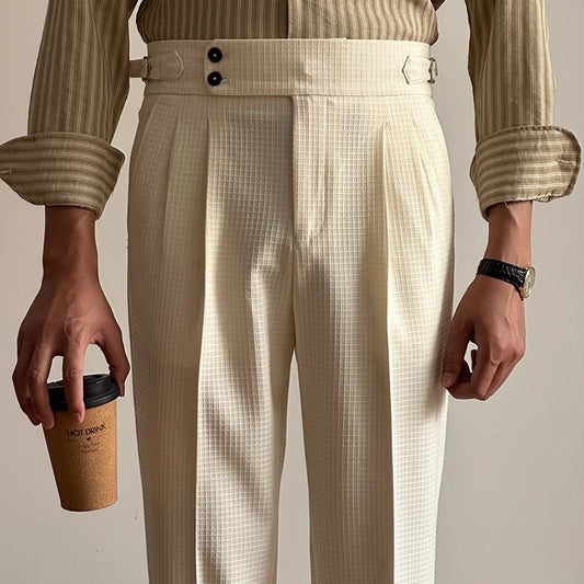 Mann in cremefarbener, karierter Anzughose mit Kaffeebecher. Elegante Herrenmode, Business-Look, gestreiftes Hemd, stilvolles Accessoire.