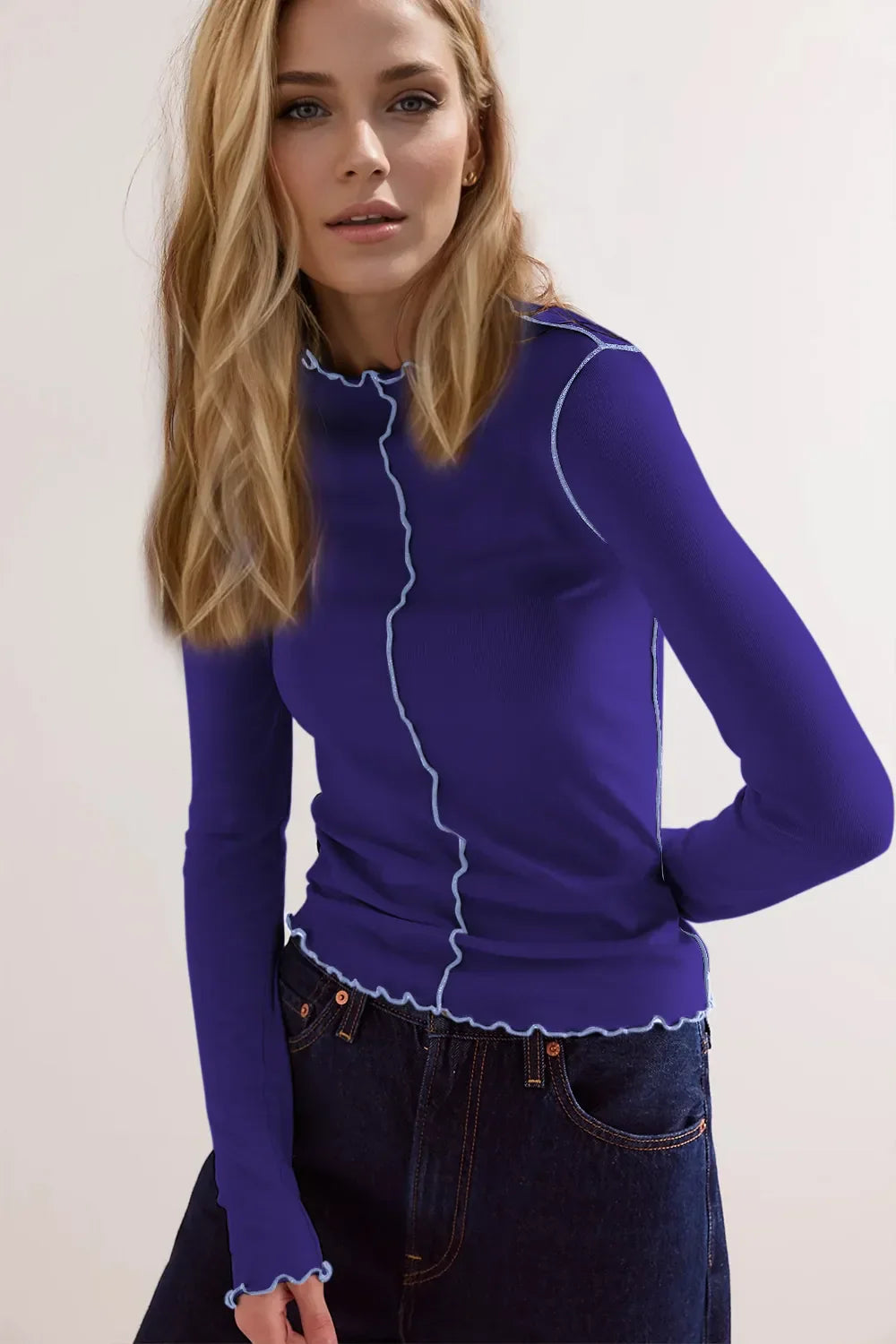 Blonde Frau in blauem, langärmligem Oberteil mit weißen Nähten, trägt dunkle Jeans. Mode, Damenbekleidung, trendiger Look.