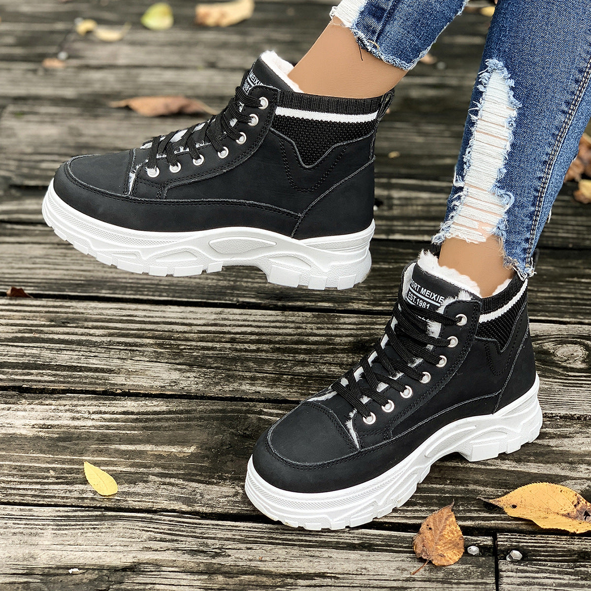 Schwarze Damen-Sneakerstiefel mit weißer Sohle auf Holzdeck, getragen mit zerrissenen Jeans. Modische Herbstschuhe, Outdoor-Style.