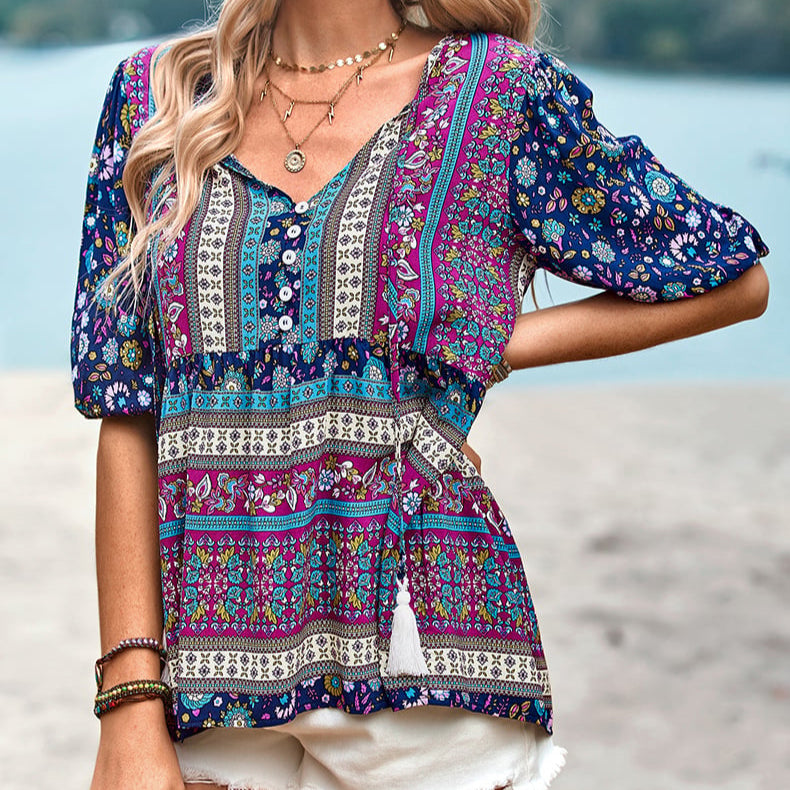 Bunte Boho-Bluse mit Blumenmuster, V-Ausschnitt und kurzen Ärmeln, getragen von einer Frau am Strand. Sommermode, lässiger Boho-Stil.