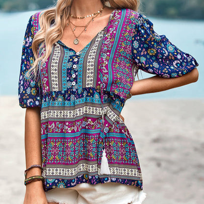 Bunte Boho-Bluse mit Blumenmuster, V-Ausschnitt und kurzen Ärmeln, getragen von einer Frau am Strand. Sommermode, lässiger Boho-Stil.