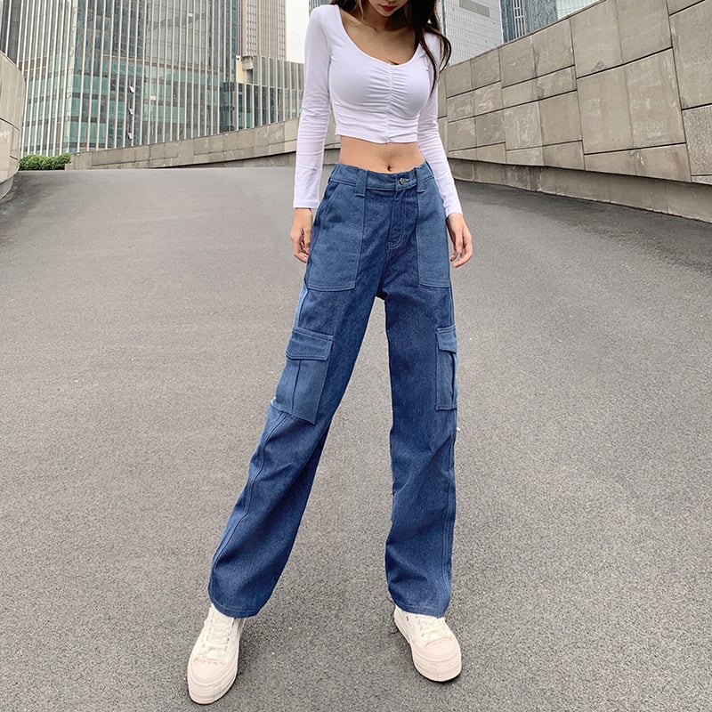 Frau in weißem Crop-Top und blauen Cargo-Jeans posiert auf städtischer Straße. Modetrend, lässiger Stil, urbane Mode, Streetwear.