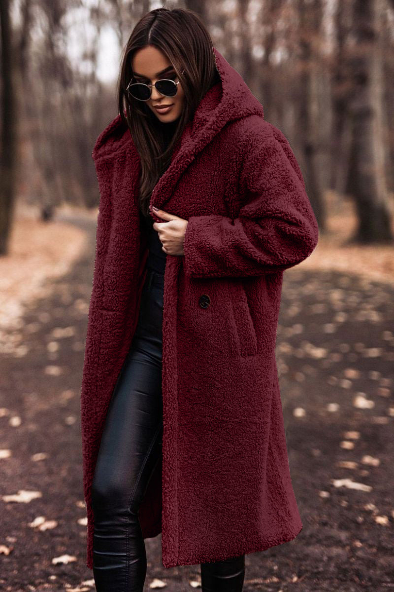 Frau im roten Teddy-Mantel und Sonnenbrille spaziert im herbstlichen Wald. Modetrend, Herbstmode, stilvoller Look, Outdoor-Bekleidung.