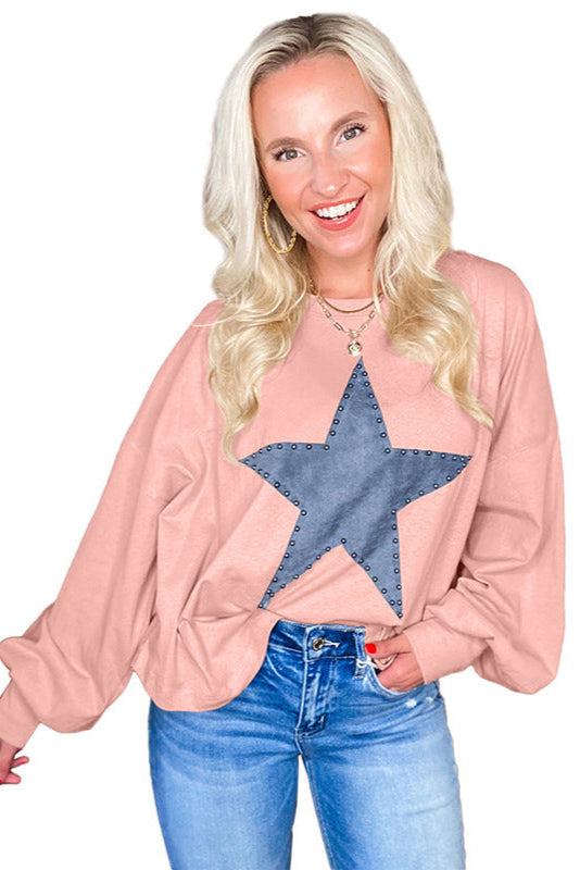 Blonde Frau in rosa Pullover mit großem Stern-Design, lächelt in die Kamera. Modetrend, lässiger Stil, Damenmode, Jeans, Schmuck.