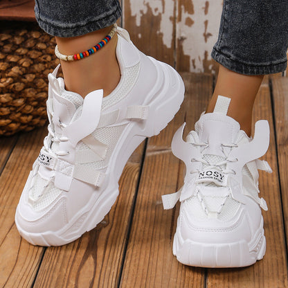 Weiße Damen-Sneaker auf Holzboden, modisches Design mit dicker Sohle und Schnürung, ideal für Freizeit und Sport, getragen mit Jeans und Fußkettchen.