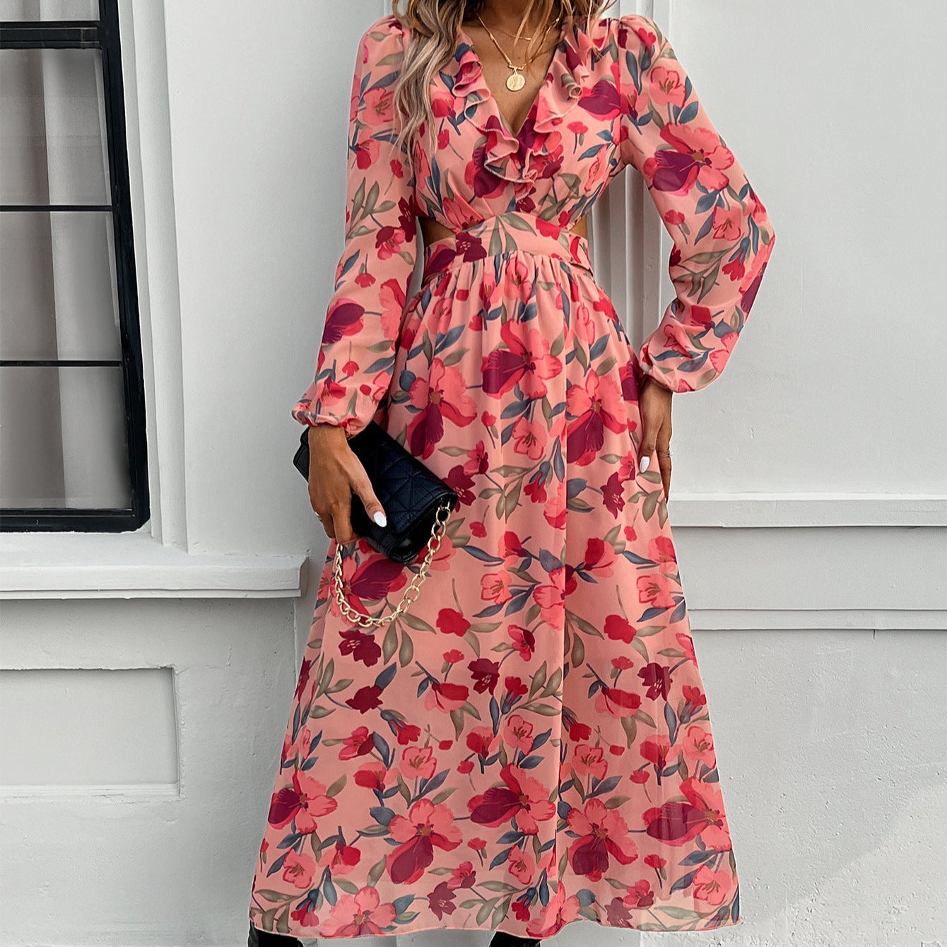 Frau in langem, geblümtem Kleid in Rosa und Rot, hält schwarze Clutch. Elegantes Outfit, modisches Design, florales Muster, Damenmode.