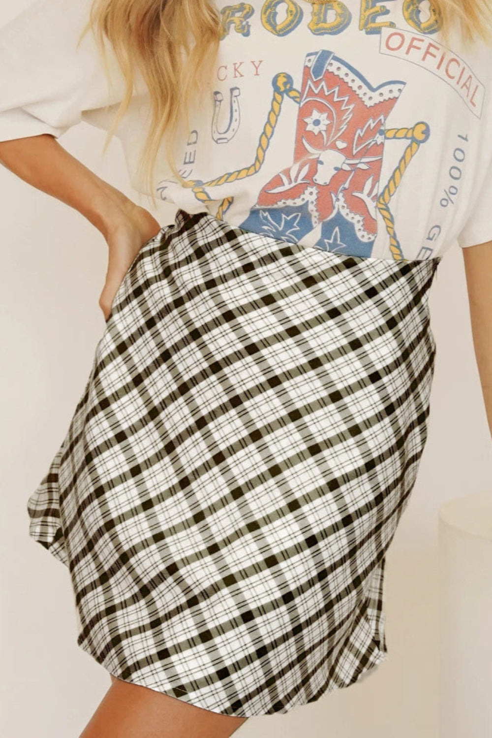 Frau trägt karierten Rock und T-Shirt mit Rodeo-Print. Modetrend, lässiger Stil, Damenmode, Sommeroutfit, Streetwear.