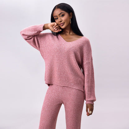 Frau in rosa Strickpullover und Hose, lächelt und posiert vor grauem Hintergrund. Modetrend, gemütlicher Strick, stilvolle Damenbekleidung.