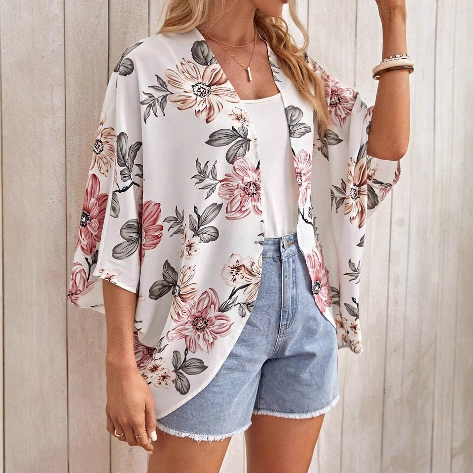 Frau trägt floralen Kimono mit rosa und grauen Blumen, kombiniert mit weißem Top und Jeansshorts. Sommermode, lässiger Stil, Damenbekleidung.