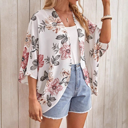 Frau trägt floralen Kimono mit rosa und grauen Blumen, kombiniert mit weißem Top und Jeansshorts. Sommermode, lässiger Stil, Damenbekleidung.