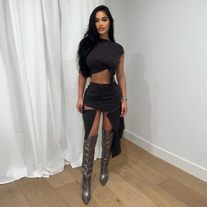 Eine Frau in einem eleganten schwarzen Kleid mit asymmetrischem Schnitt und hohen silbernen Stiefeln steht vor einem weißen Vorhang.