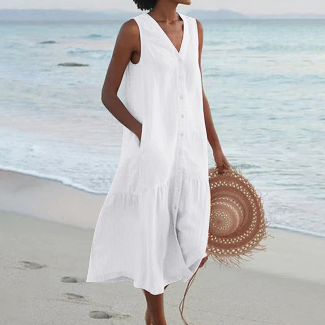 Frau in weißem Sommerkleid am Strand, hält Strohhut. Strandmode, ärmelloses Kleid, Sommeroutfit, Meereshintergrund.