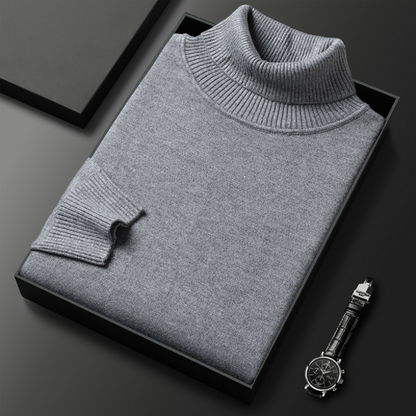 Grauer Rollkragenpullover aus Kaschmir in Geschenkbox, elegant gefaltet, neben einer stilvollen Armbanduhr auf schwarzem Hintergrund.