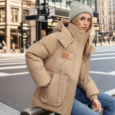 Frau in beiger Daunenjacke und grauer Mütze sitzt auf einer Bank in der Stadt. Wintermode, urbane Kleidung, stilvolle Damenbekleidung.