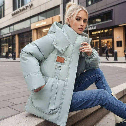 Blonde Frau in hellblauer Daunenjacke sitzt auf Bürgersteig, moderne Stadtumgebung, Wintermode, stilvolle Kleidung, urbane Kulisse.