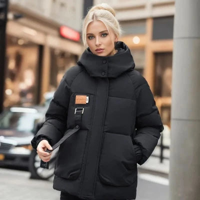 Blonde Frau in schwarzer Daunenjacke mit Kapuze, steht auf städtischer Straße. Wintermode, warme Kleidung, stilvolle Damenjacke, urbane Umgebung.