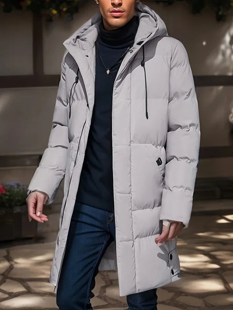 Mann in grauem Daunenmantel mit Kapuze, schwarzem Rollkragenpullover und blauer Jeans. Wintermode, stilvolle Herrenbekleidung, Outdoor-Jacke.