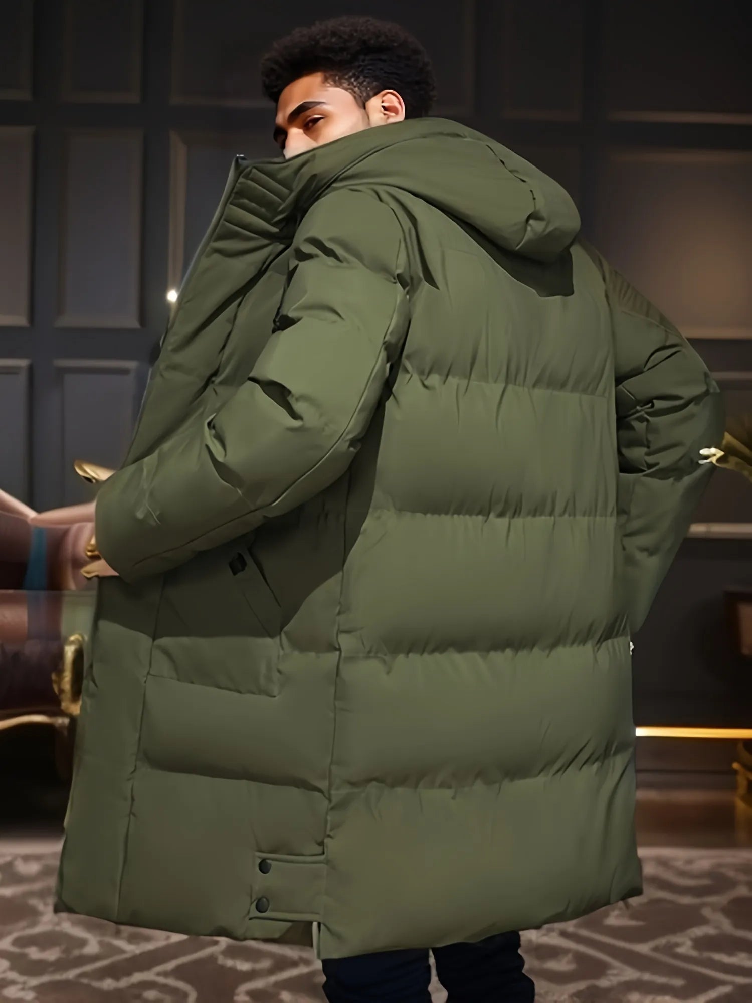 Junger Mann in olivgrünem Daunenmantel mit Kapuze, steht in modernem Raum. Wintermode, Herrenbekleidung, stilvoller Mantel, warme Jacke.