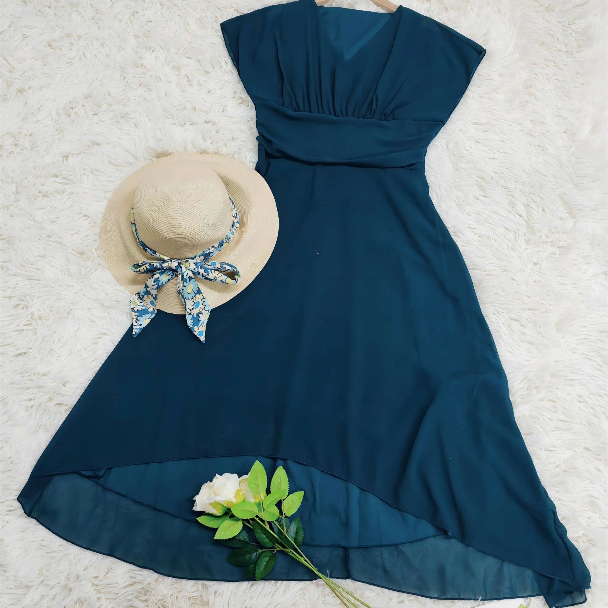 Blaues Sommerkleid mit V-Ausschnitt auf weißem Hintergrund, kombiniert mit Strohhut und Rose. Elegantes Damenoutfit, ideal für warme Tage.