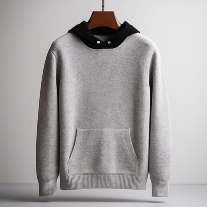 Grauer Kapuzenpullover aus Baumwolle mit Kängurutasche, hängend auf Holzkleiderbügel. Minimalistisches Design, modische Freizeitkleidung.