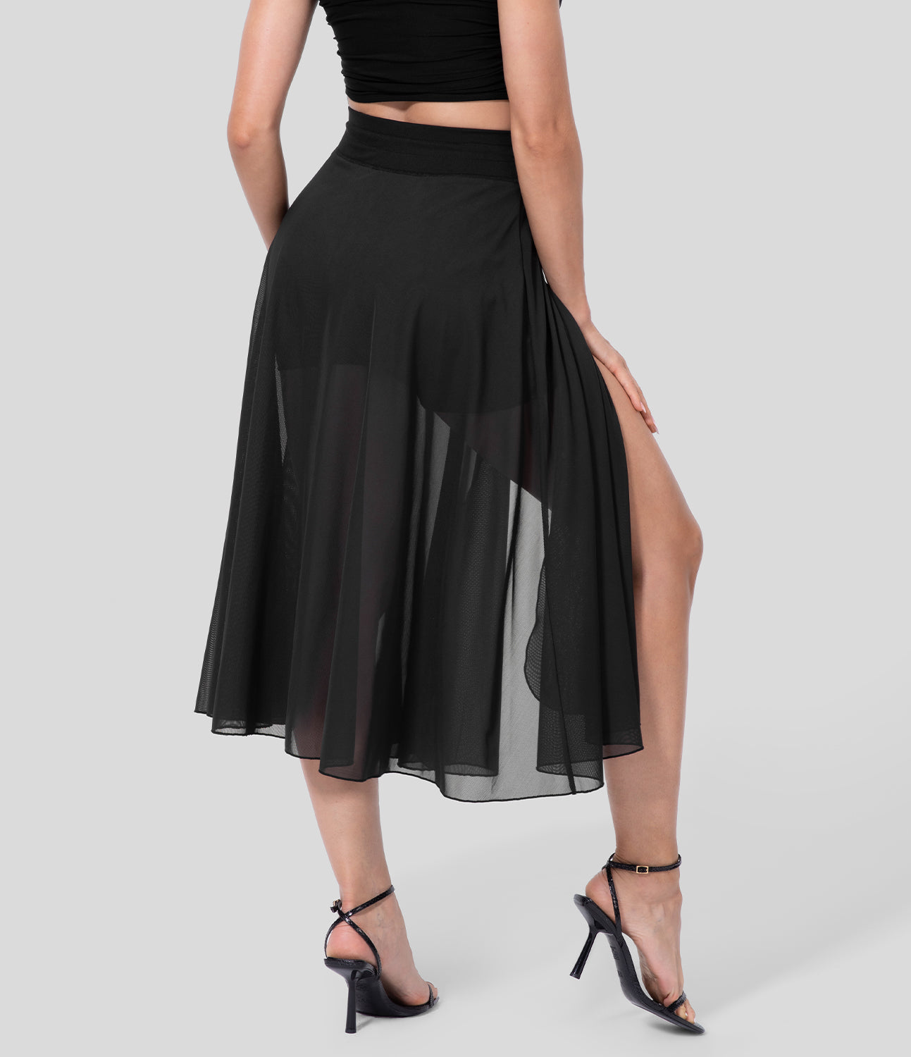 Frau in schwarzem, transparentem Maxirock mit hohem Schlitz, kombiniert mit schwarzen High Heels. Elegante Damenmode, stilvoller Look.
