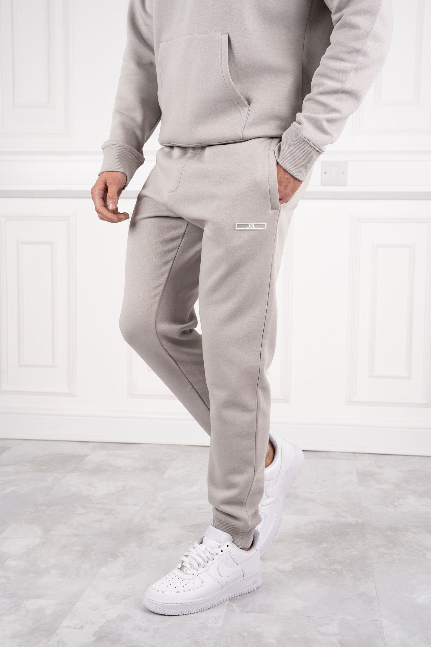 Mann in grauem Jogginganzug und weißen Sneakers vor weißer Wand. Bequeme Sportbekleidung, modischer Freizeitlook, Herrenmode.