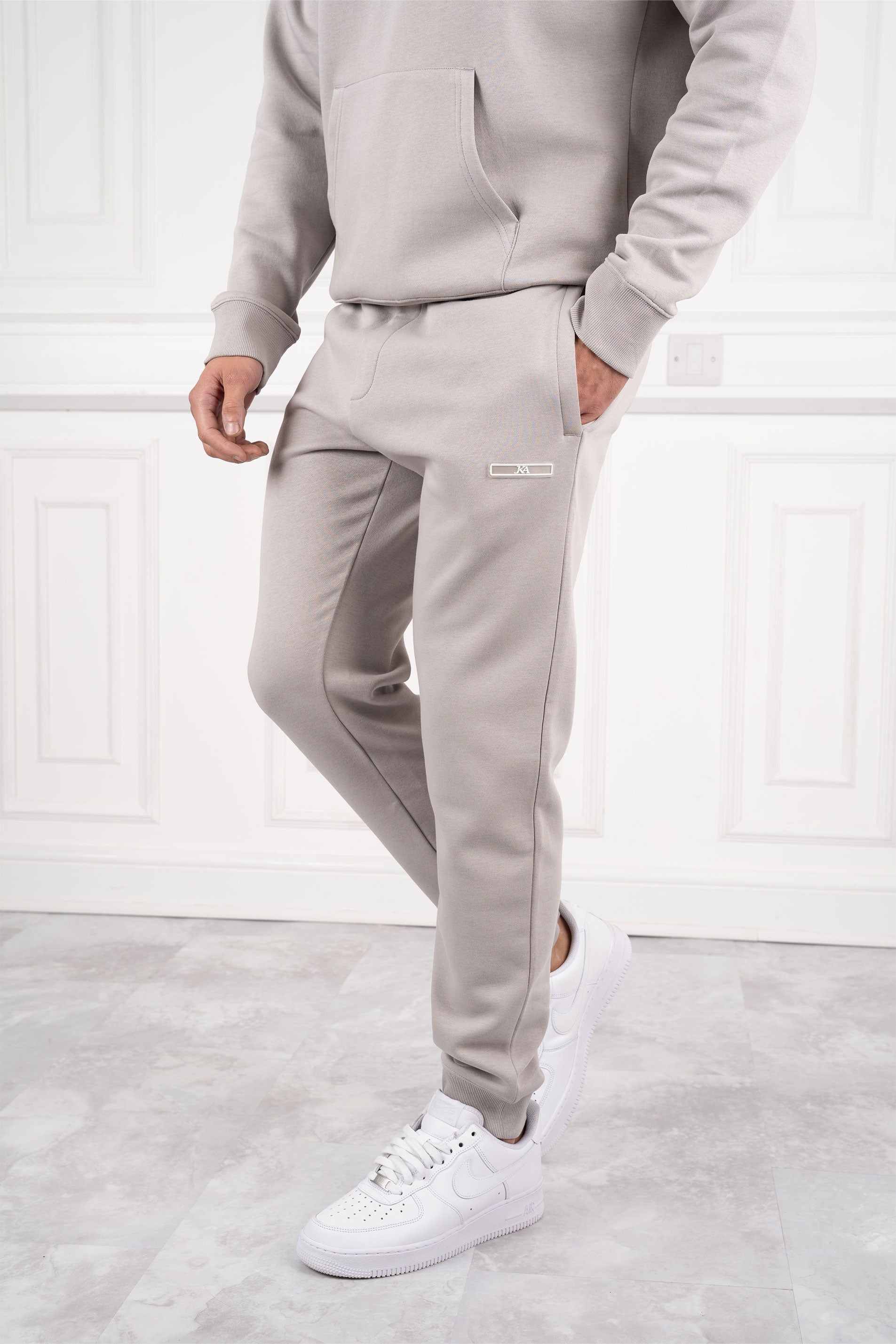 Mann in grauem Jogginganzug und weißen Sneakers vor weißer Wand. Bequeme Sportbekleidung, modischer Freizeitlook, Herrenmode.