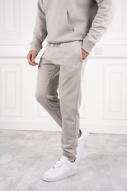 Mann in grauem Jogginganzug und weißen Sneakers vor weißer Wand. Bequeme Sportbekleidung, modischer Freizeitlook, Herrenmode.