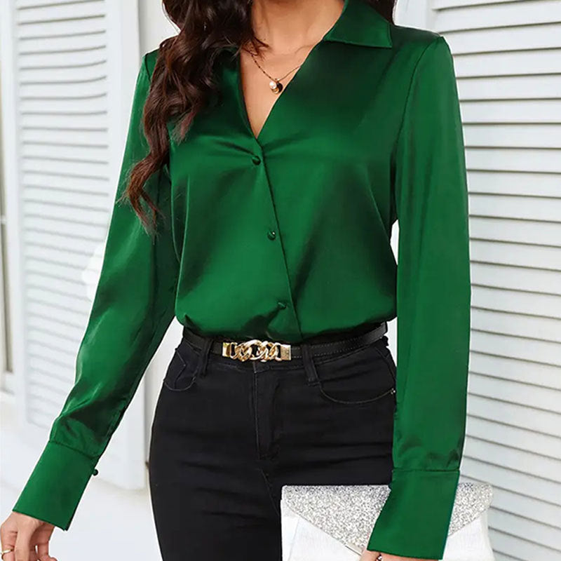 Frau in grüner Bluse und schwarzer Hose, hält silberne Clutch. Elegante Mode, stilvolle Damenbekleidung, modernes Outfit für Büro oder Abend.