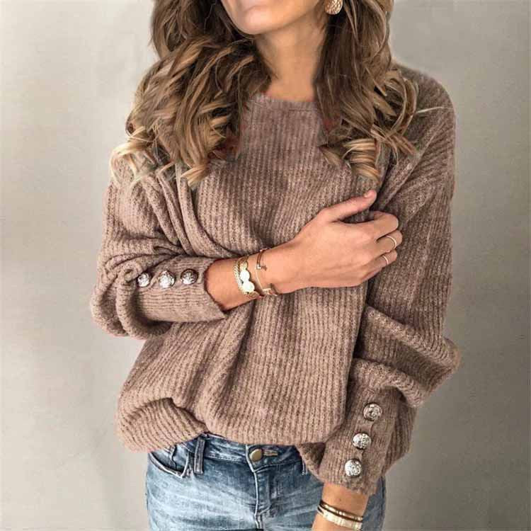 Frau in beigem Strickpullover mit Knöpfen an den Ärmeln, trägt Jeans und Armbänder. Modetrend Herbst, gemütlicher Look, Damenmode.