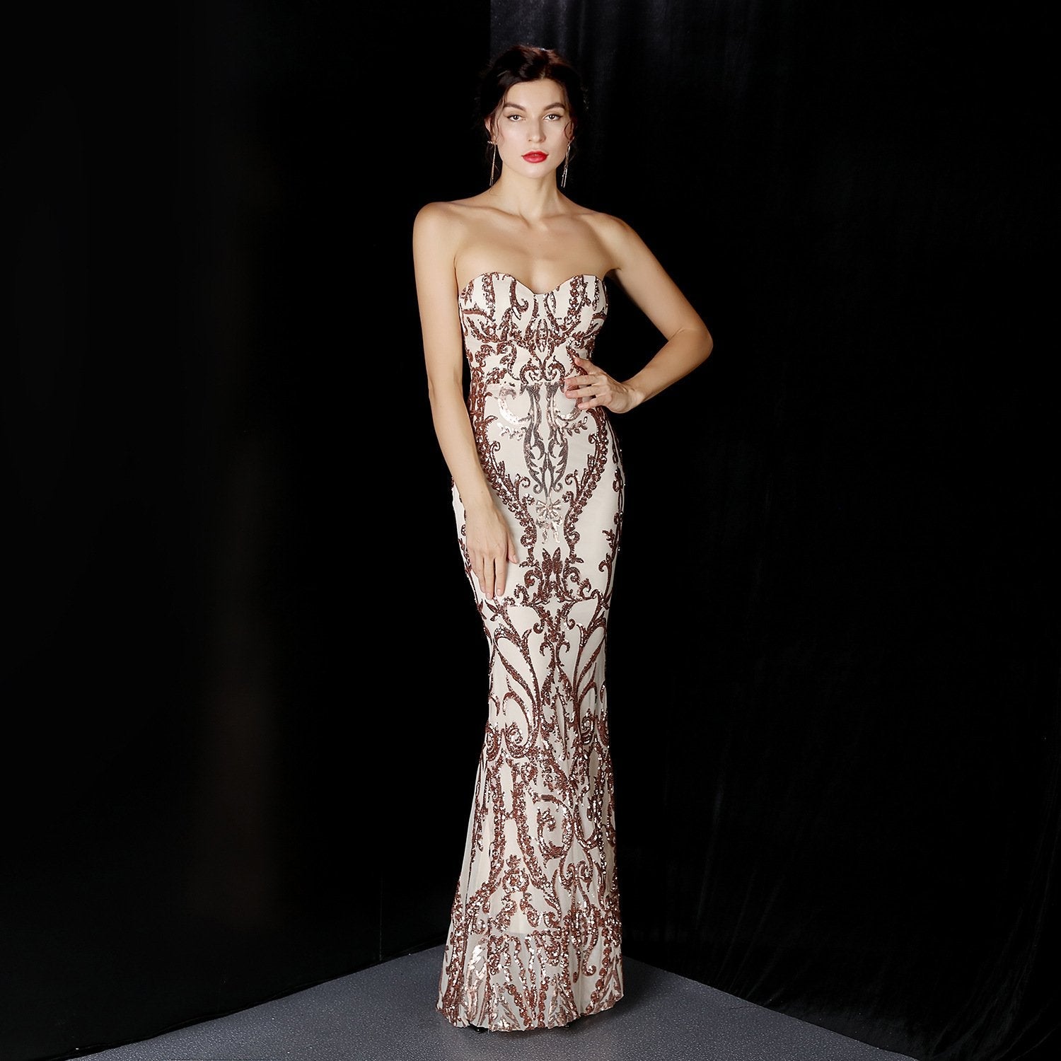 Frau in eleganter, schulterfreier Abendkleid mit aufwendigem Muster, posiert vor schwarzem Hintergrund. Perfekt für Gala, Ball oder Abendveranstaltung.