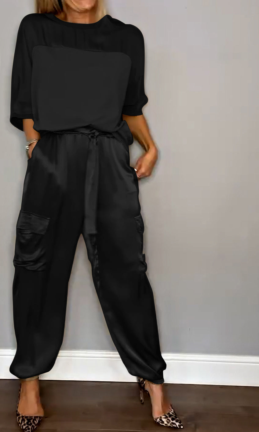 Frau in schwarzem Jumpsuit mit Taschen, steht vor grauer Wand, trägt Leoparden-High-Heels. Modetrend, eleganter Look, Damenbekleidung.