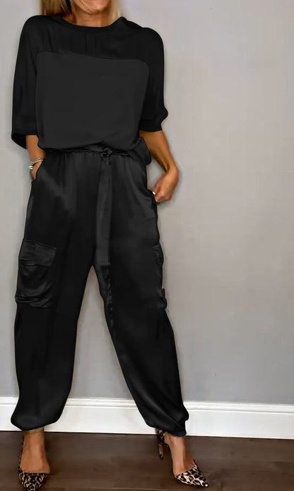Frau in schwarzem Jumpsuit mit Taschen, steht vor grauer Wand, trägt Leoparden-High-Heels. Modetrend, eleganter Look, Damenbekleidung.