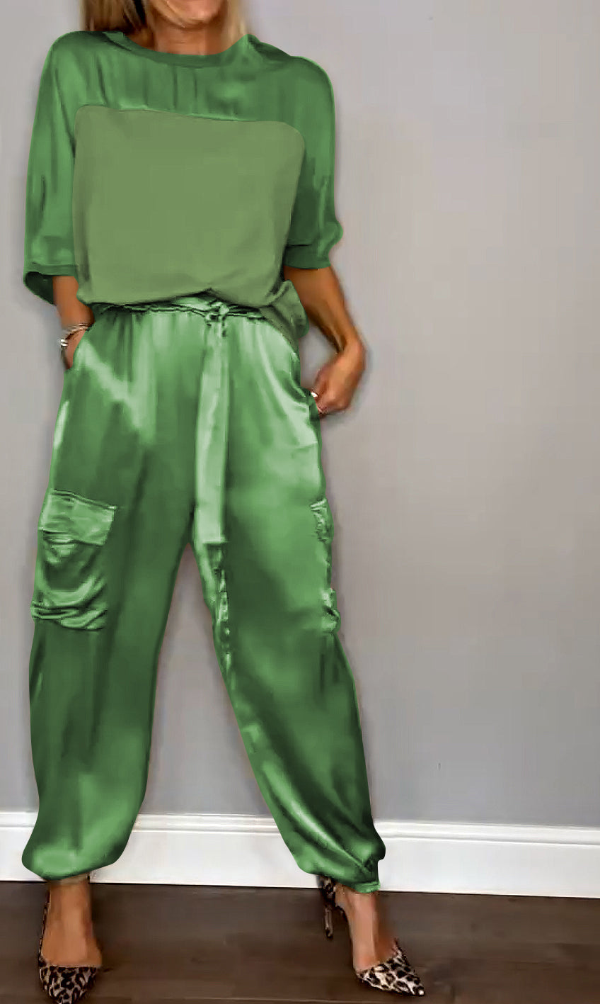 Frau in grüner Satin-Hose und passendem Oberteil vor grauer Wand, trägt Leoparden-High-Heels. Elegante Damenmode, stilvoller Look.
