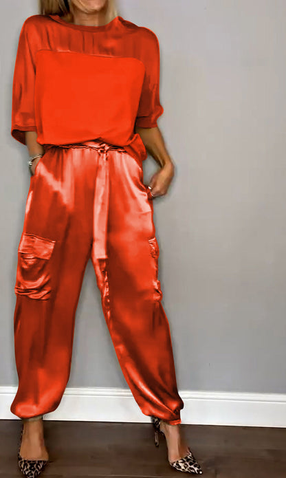 Frau in rotem Satin-Outfit mit lockerem Oberteil und Hose, kombiniert mit Leoparden-High-Heels, vor grauer Wand stehend. Fashion, Eleganz, Stil.