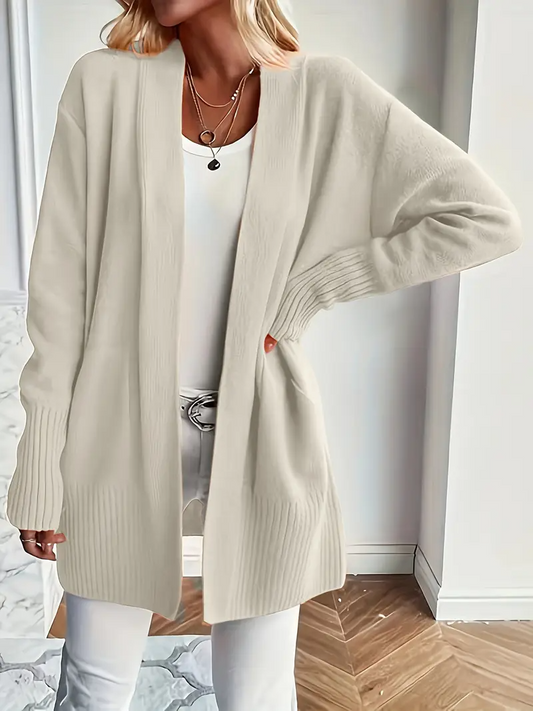 Frau in beigem Strick-Cardigan und weißem Top, modisch kombiniert mit weißer Hose. Eleganter Look, ideal für Herbstmode und lässige Outfits.
