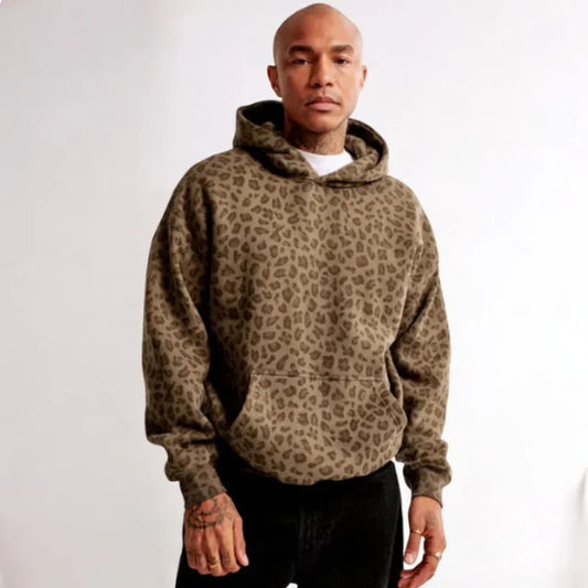 Mann in braunem Leopardenmuster-Hoodie, lässiger Stil, weiße Wand im Hintergrund, Mode für Herren, trendige Streetwear, komfortabel und modern.