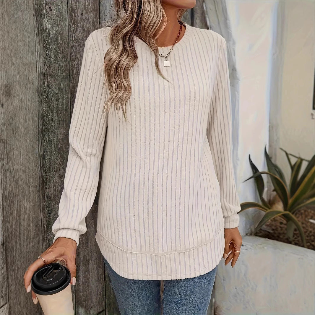 Frau in weißem, gestreiftem Pullover und blauer Jeans hält einen Kaffeebecher. Lässige Herbstmode, Outdoor-Hintergrund mit Pflanzen.