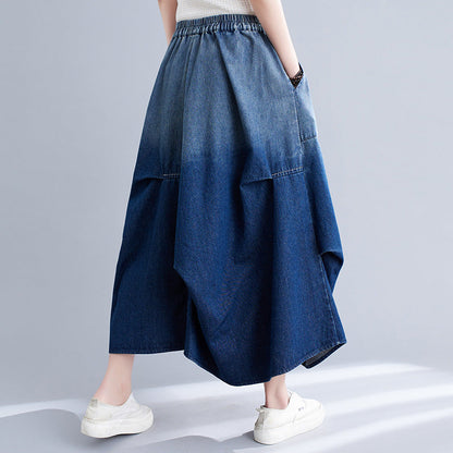 Frau trägt langen, weiten Jeansrock in Blau mit elastischem Bund, kombiniert mit weißen Sneakers. Modetrend, Damenbekleidung, lässiger Stil.