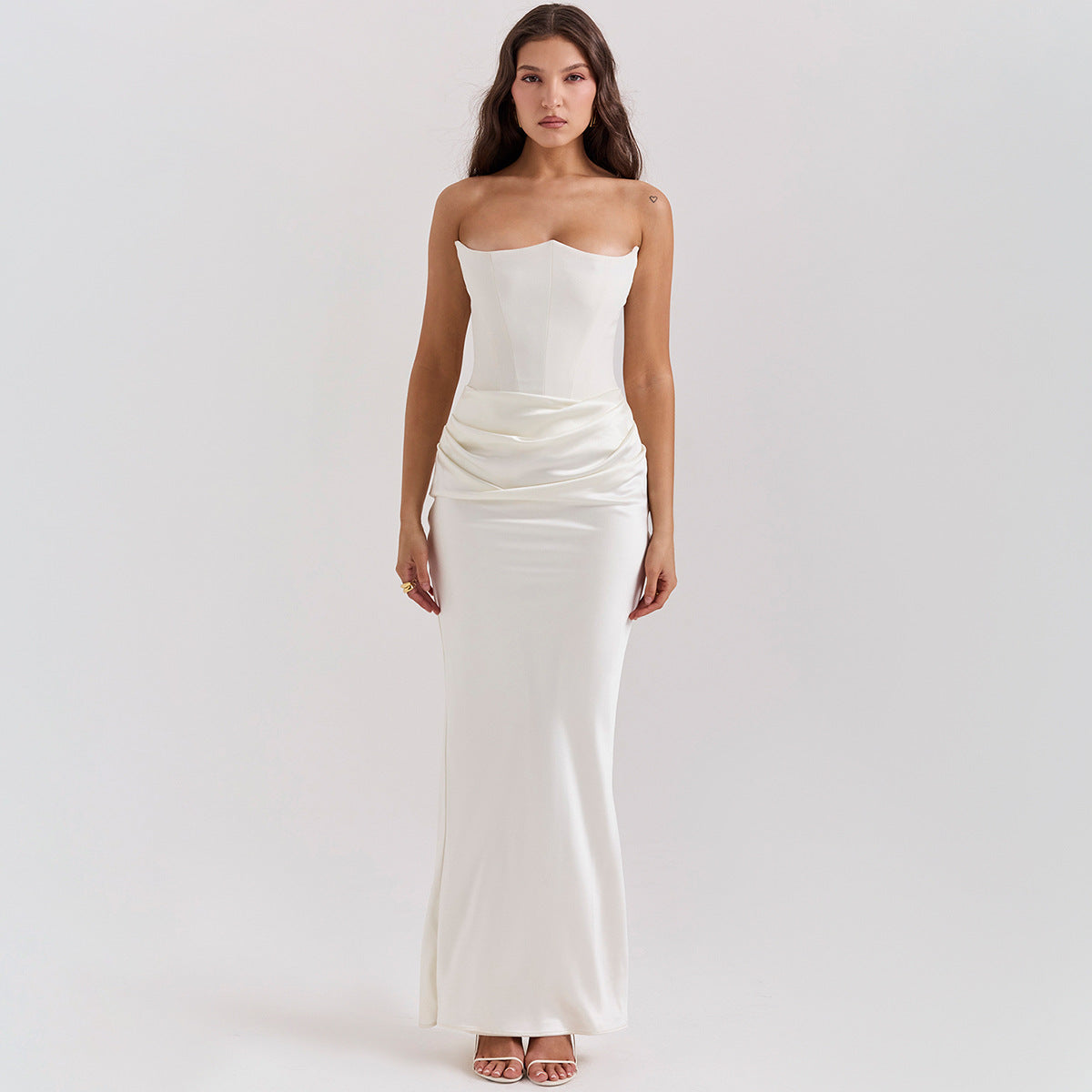 Frau in elegantem, trägerlosem weißen Abendkleid mit drapiertem Rock, stehend vor neutralem Hintergrund. Perfekt für Hochzeiten oder formelle Anlässe.