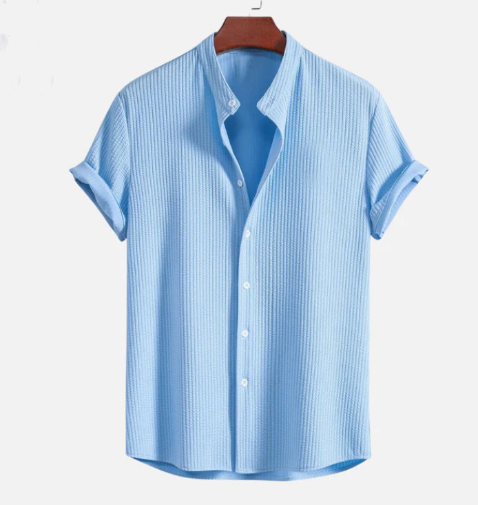 Hellblaues Herrenhemd mit Stehkragen, kurzen Ärmeln und Knopfleiste auf Holzkleiderbügel. Sommermode, Herrenbekleidung, Freizeitlook.