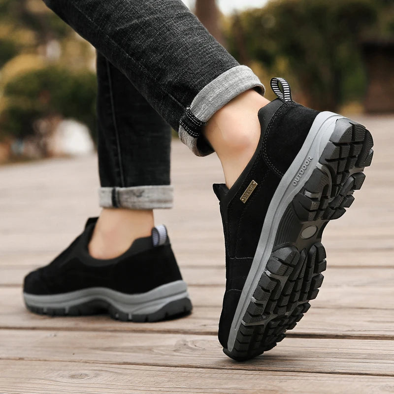 Schwarze Outdoor-Wanderschuhe mit rutschfester Sohle auf Holzweg, getragen von Person in hochgekrempelten Jeans. Ideal für Trekking und Outdoor-Aktivitäten.