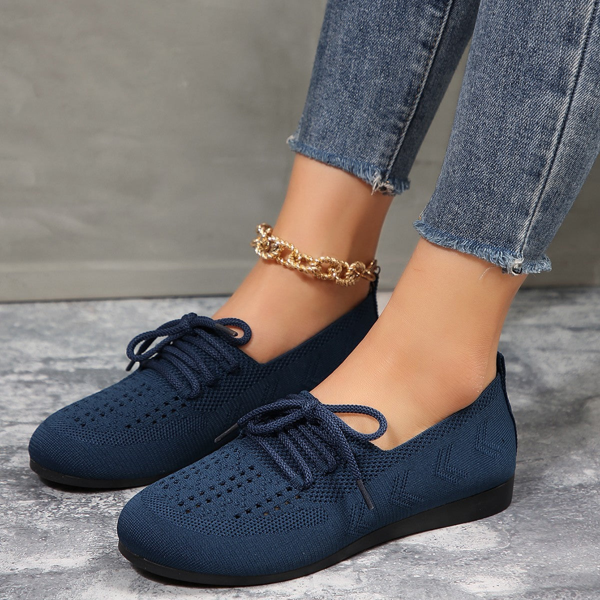 Damenfüße in blauen Strick-Sneakern mit goldener Fußkette, Jeans. Modische, bequeme Schuhe, ideal für Freizeit und Alltag.