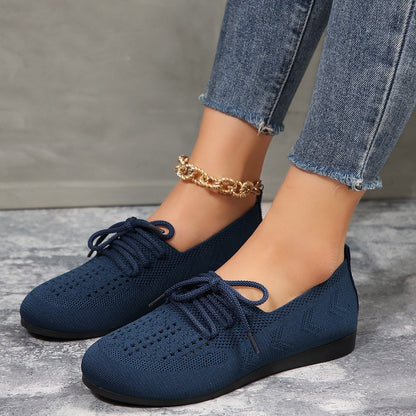 Damenfüße in blauen Strick-Sneakern mit goldener Fußkette, Jeans. Modische, bequeme Schuhe, ideal für Freizeit und Alltag.