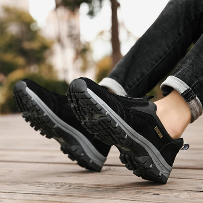 Schwarze Outdoor-Wanderschuhe mit robustem Profil auf Holzdeck, getragen von Person in Jeans. Ideal für Trekking und Outdoor-Aktivitäten.